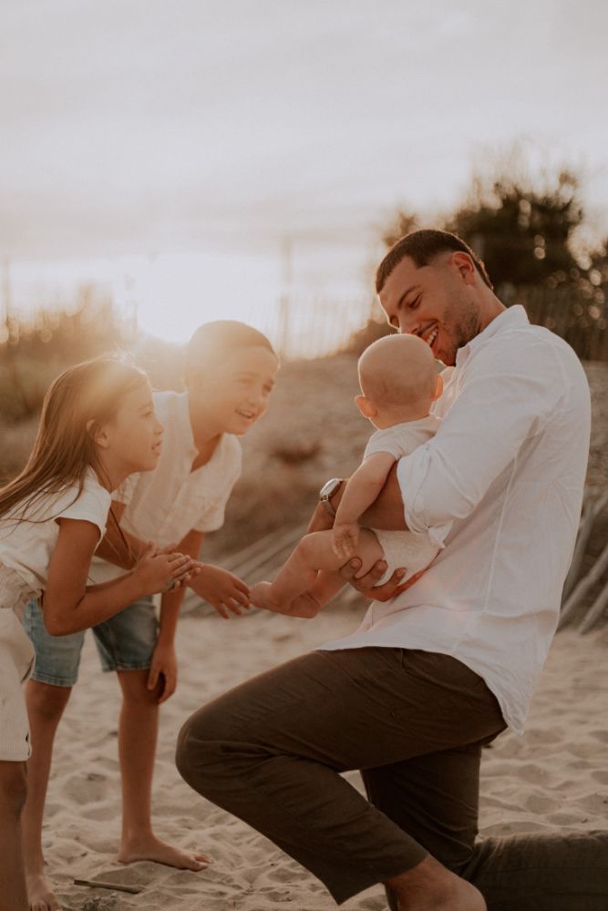 Un père tend son bébé vers ses aînés, au soleil couchant