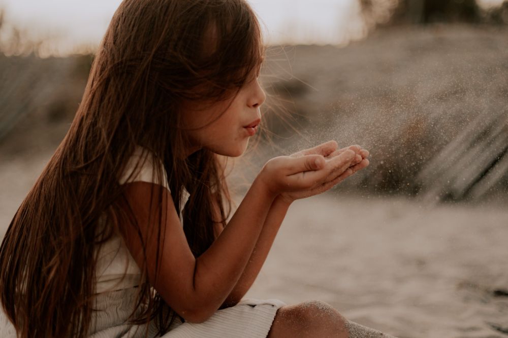 Une fillette souffle du sable au creux de ses mains