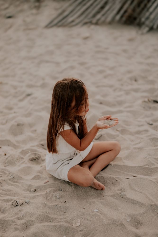 Une fillette assise de dos, sable au creux de la main