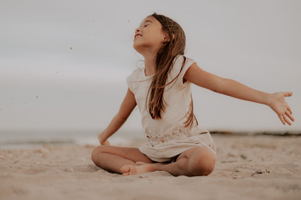Une enfant assise dans le sable, bras ouverts