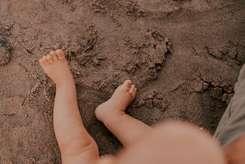 Jambes et pieds d'un bébé posés sur le sable