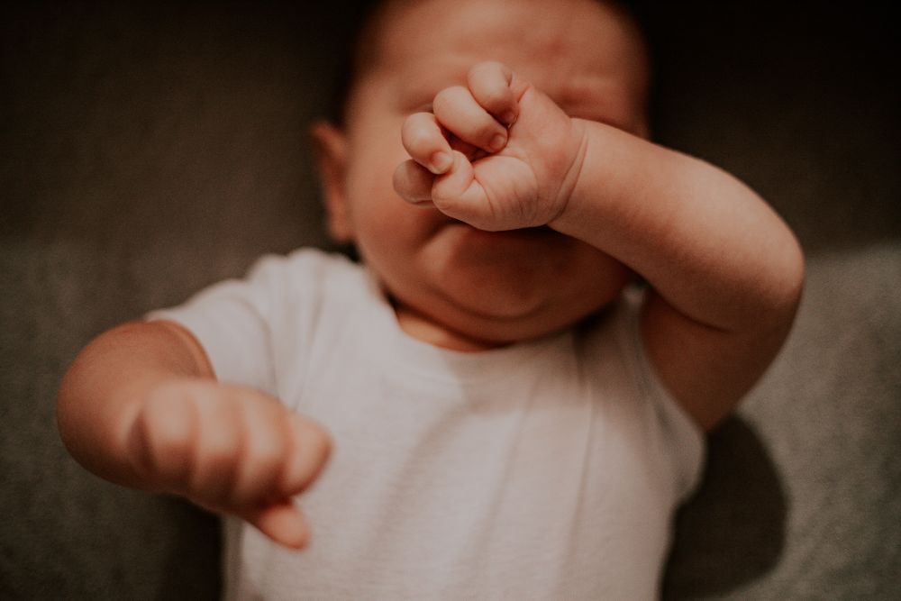 Un bébé se frotte les yeux, poings serrés