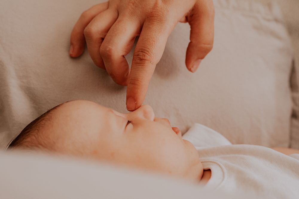 Un doigt effleure le nez d'un bébé endormi